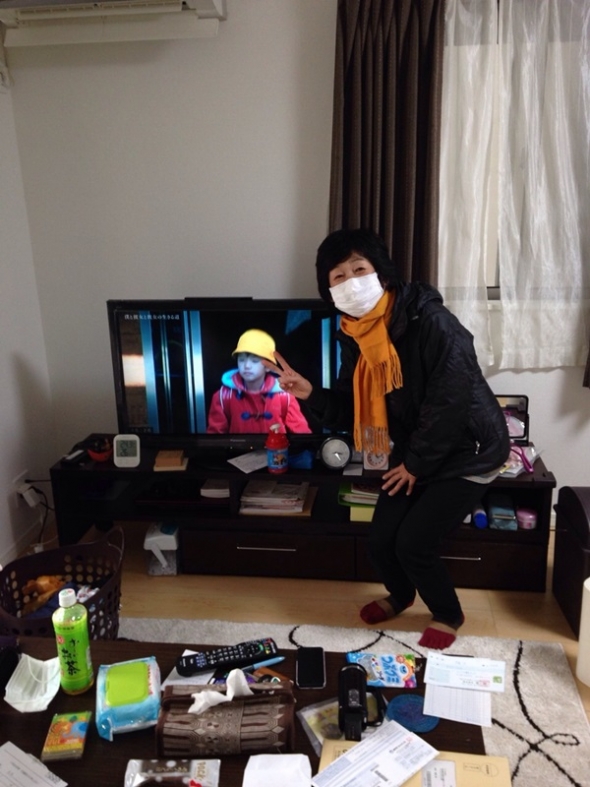 テレビ前のマスク姿でピースサインを作る女性