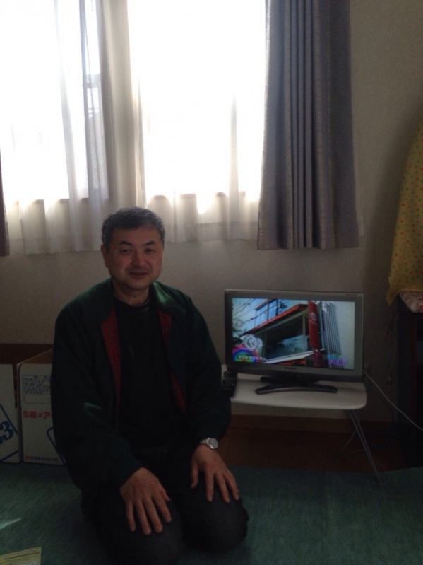 テレビ横で腰かけている男性