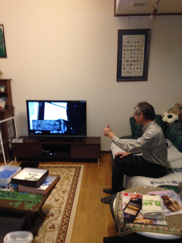 ソファーに腰かけてグッズサインを示す男性