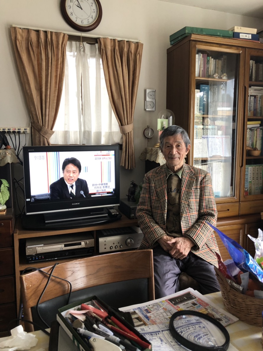 テレビ横に腰かけた男性