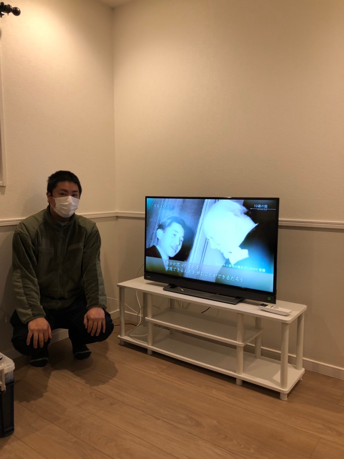 テレビの横でしゃがむ男性
