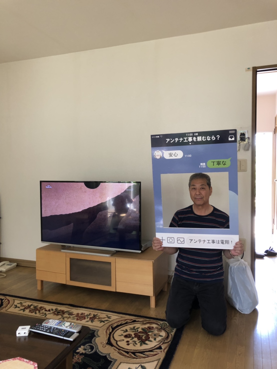 テレビ横でパネルを手にして撮影に応じる男性