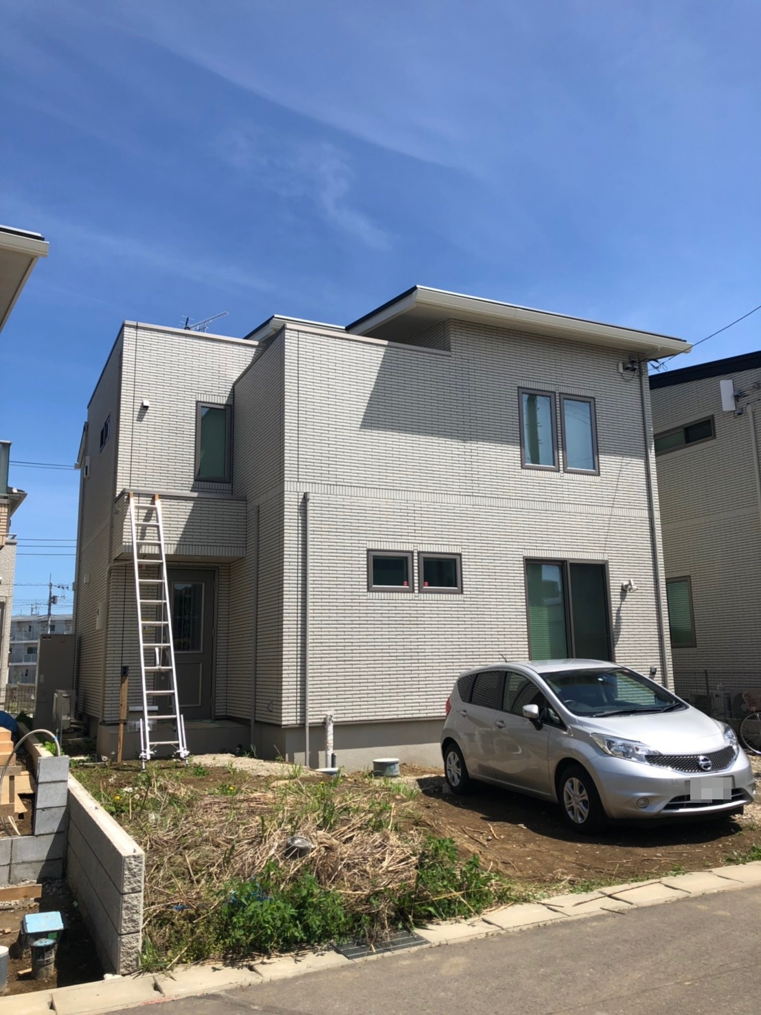 梯子を立てかけた戸建住宅と庭に停めた乗用車