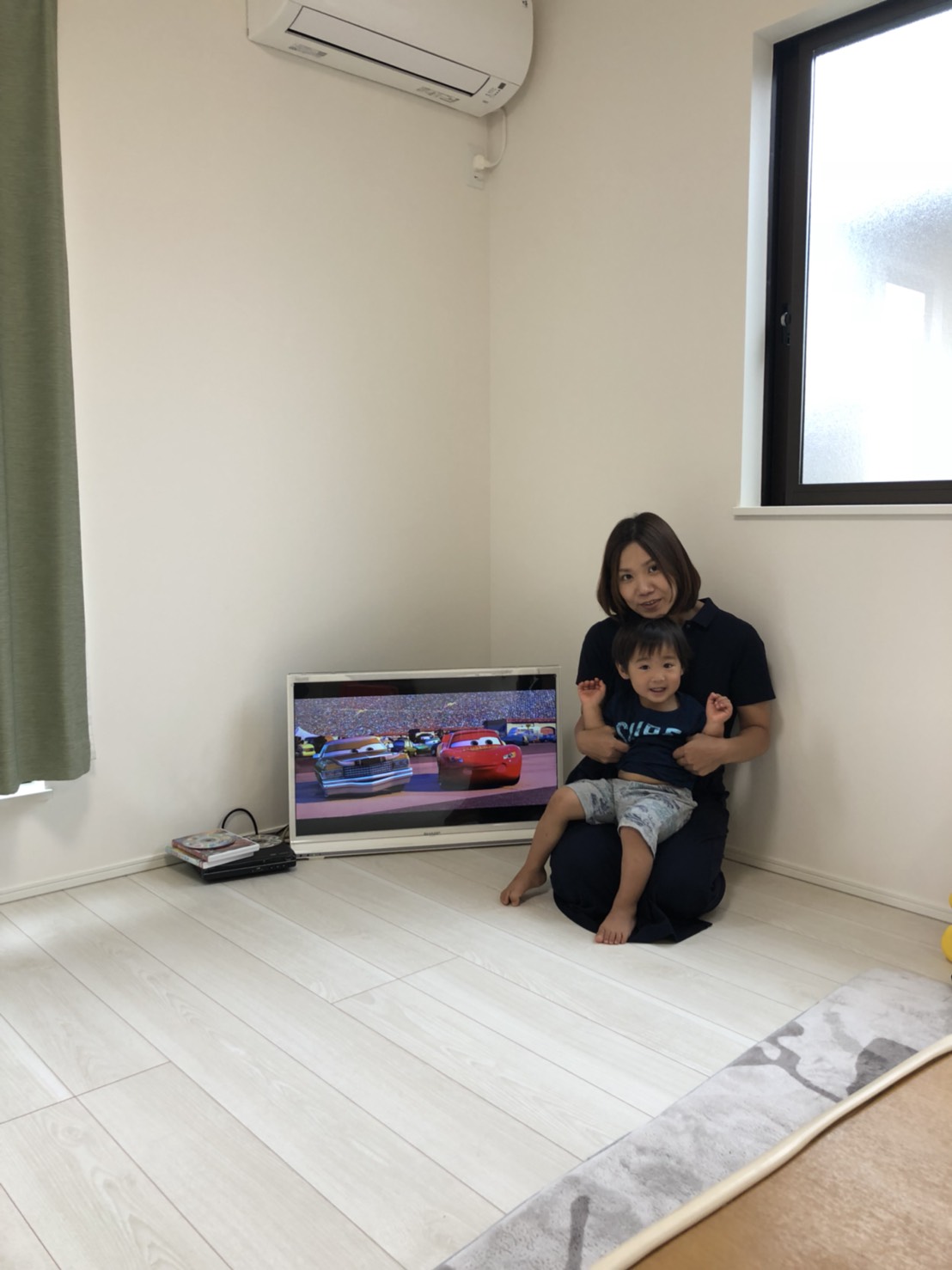 テレビ横で座って撮影に応じる親子