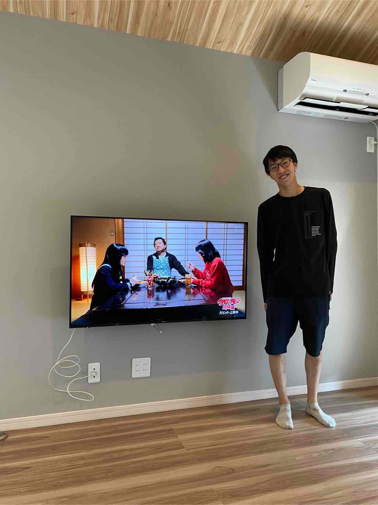 壁掛けテレビ横に立つ男性